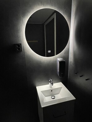 Een badkamer met een ronde spiegel, een wit wastafelmeubel en een zeepdispenser.