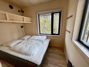 Un dormitorio con cama, ventana que da a árboles y estante de madera sobre la cama.