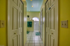 Un pasillo con puertas blancas, suelo de baldosas y pared verde.