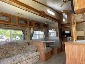 A compact RV interior with a sofa, a dining area, and a TV. - Vacation RV Rental Near Disney with Pool (Kissimmee)