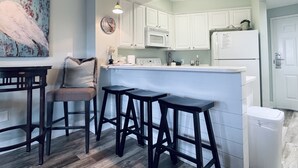 A modern kitchen with white cabinets, a white refrigerator, and a bar area with stools. - 1BR/1.5BA retreat with direct beach access (Orange Beach)