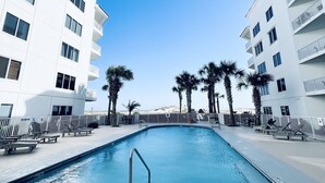 A swimming pool surrounded by lounge chairs and palm trees, with white buildings in the background. - 1BR/1.5BA retreat with direct beach access (Orange Beach)