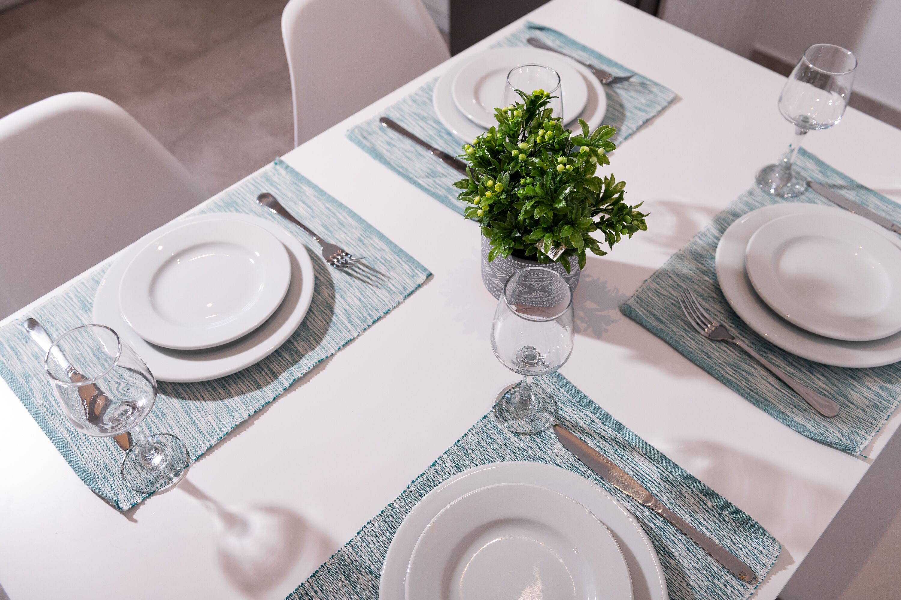 A neatly set dining table with white plates, silverware, and a small potted plant.