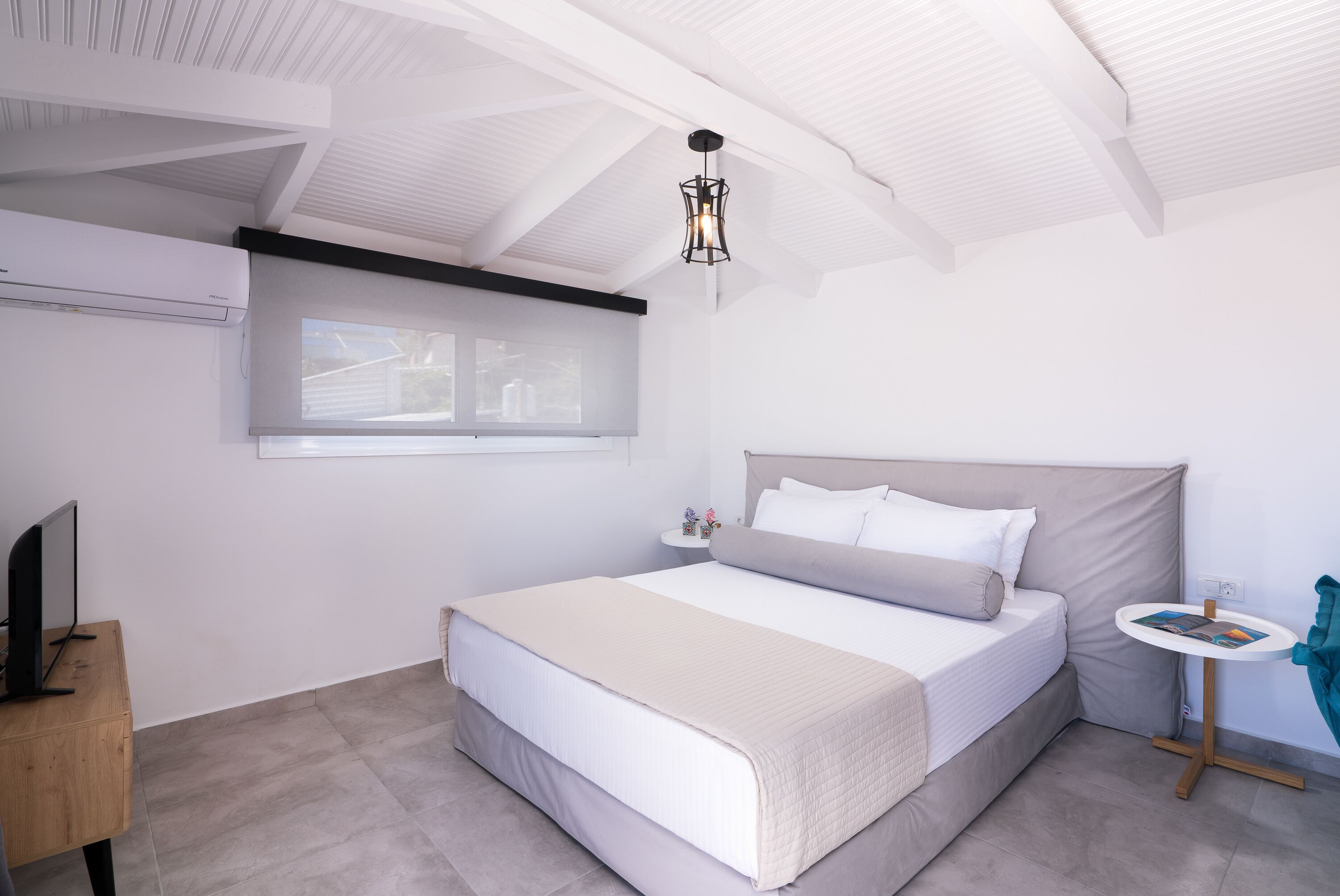 A bedroom with a bed, a small bedside table, a TV, and a window.