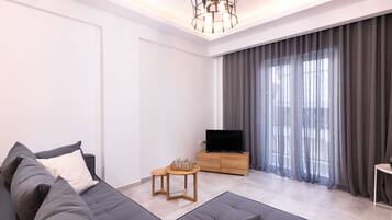 A modern living room with a grey sofa, a wooden TV stand, and a large window with grey curtains.