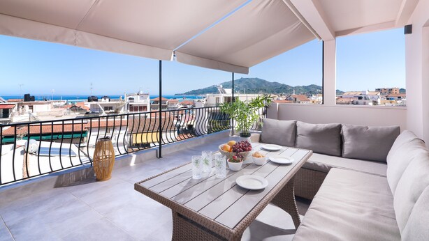 A balcony with a view of the sea and mountains, furnished with a sofa, table, and dining setup. - Lithies Zante Living (Zakynthos)