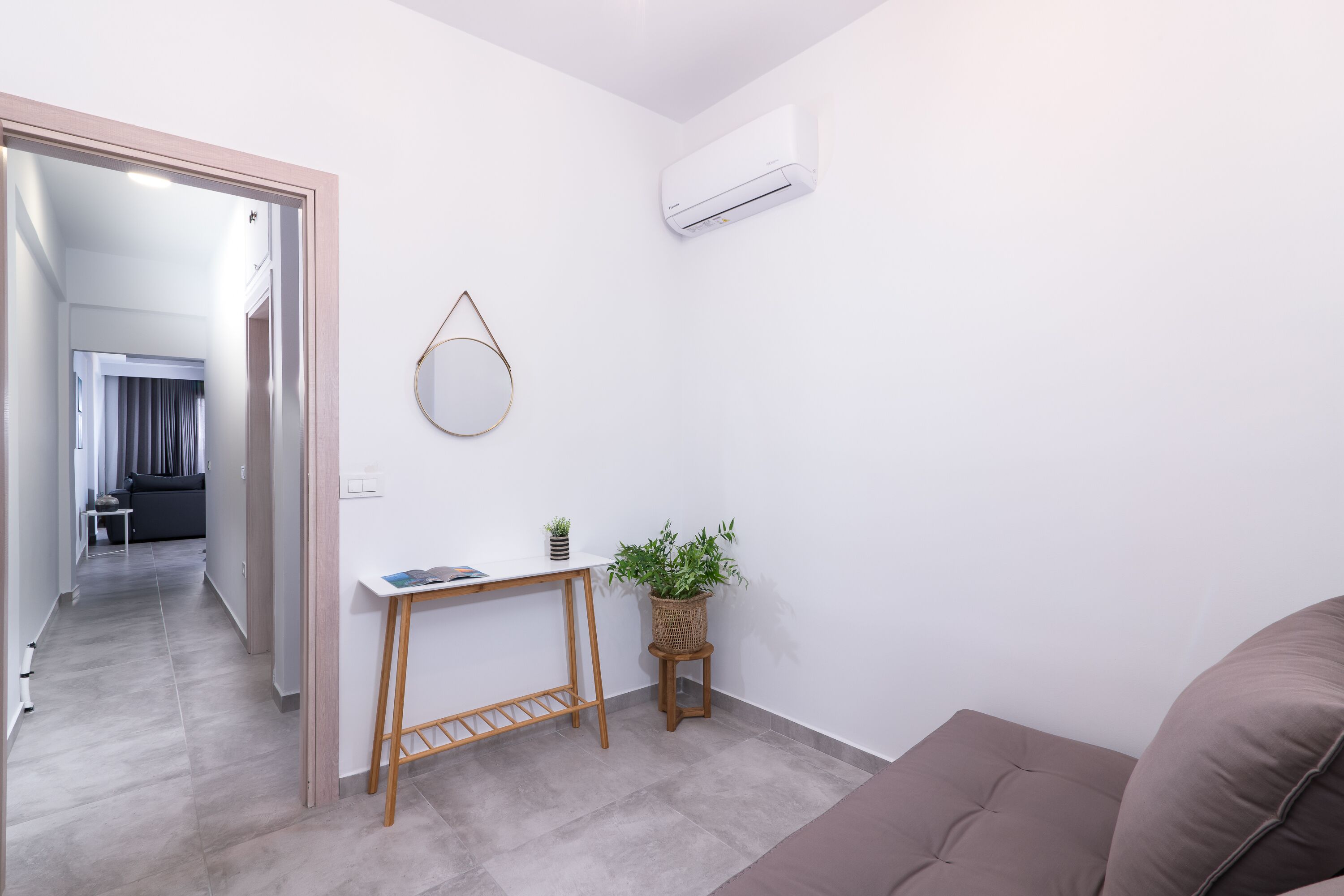 Un salón moderno con un sofá gris, una pequeña mesa de madera con una planta, y un aire acondicionado instalado en la pared.