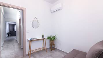 Un salón moderno con un sofá gris, una pequeña mesa de madera con una planta, y un aire acondicionado instalado en la pared.