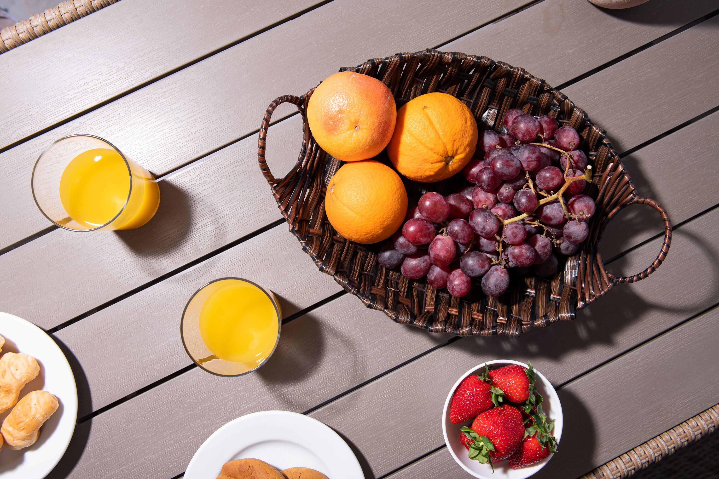 A wicker basket filled with oranges and grapes on a wooden table.