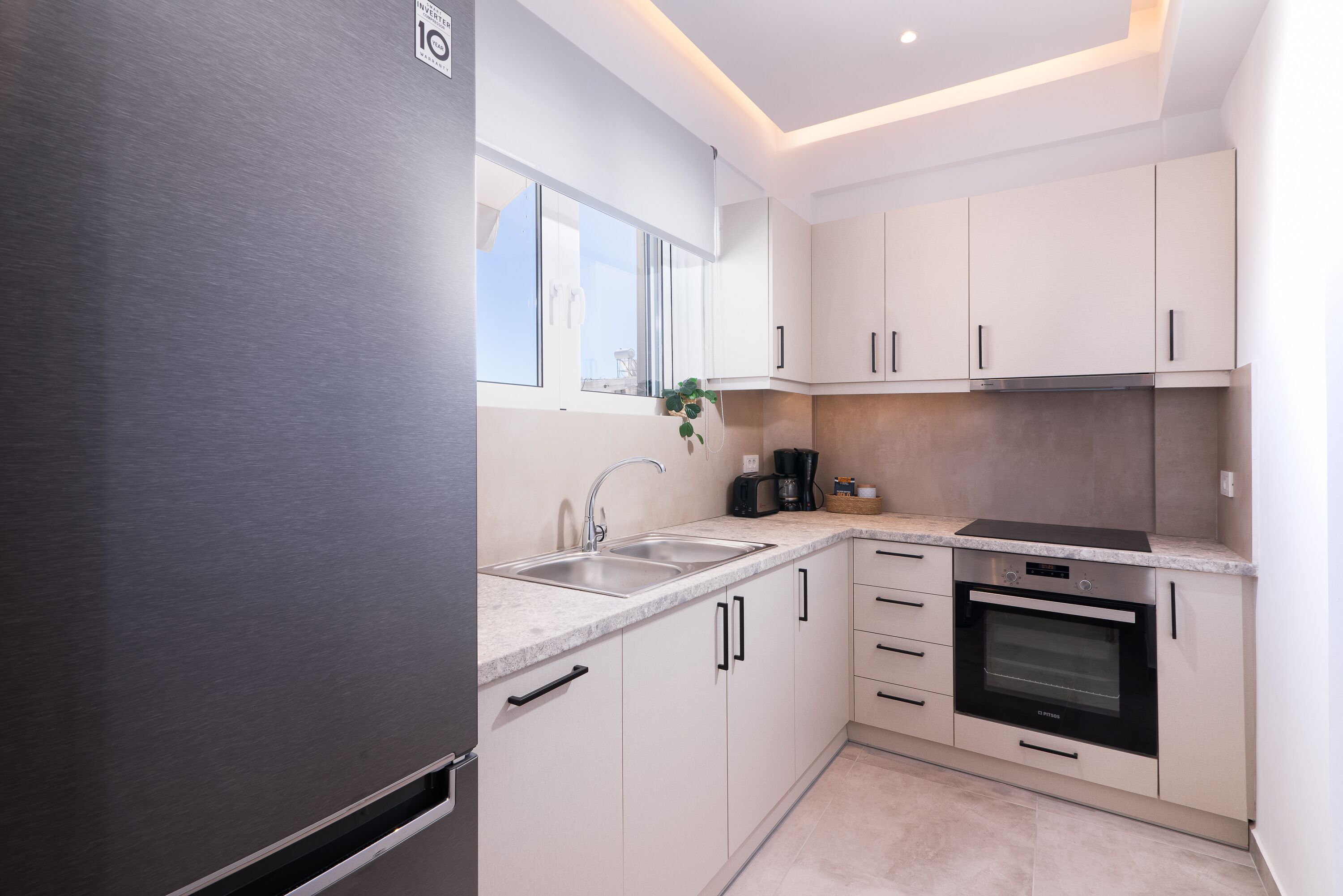 Una cocina moderna con armarios blancos, electrodomésticos de acero inoxidable y un ventanal que proporciona luz natural.