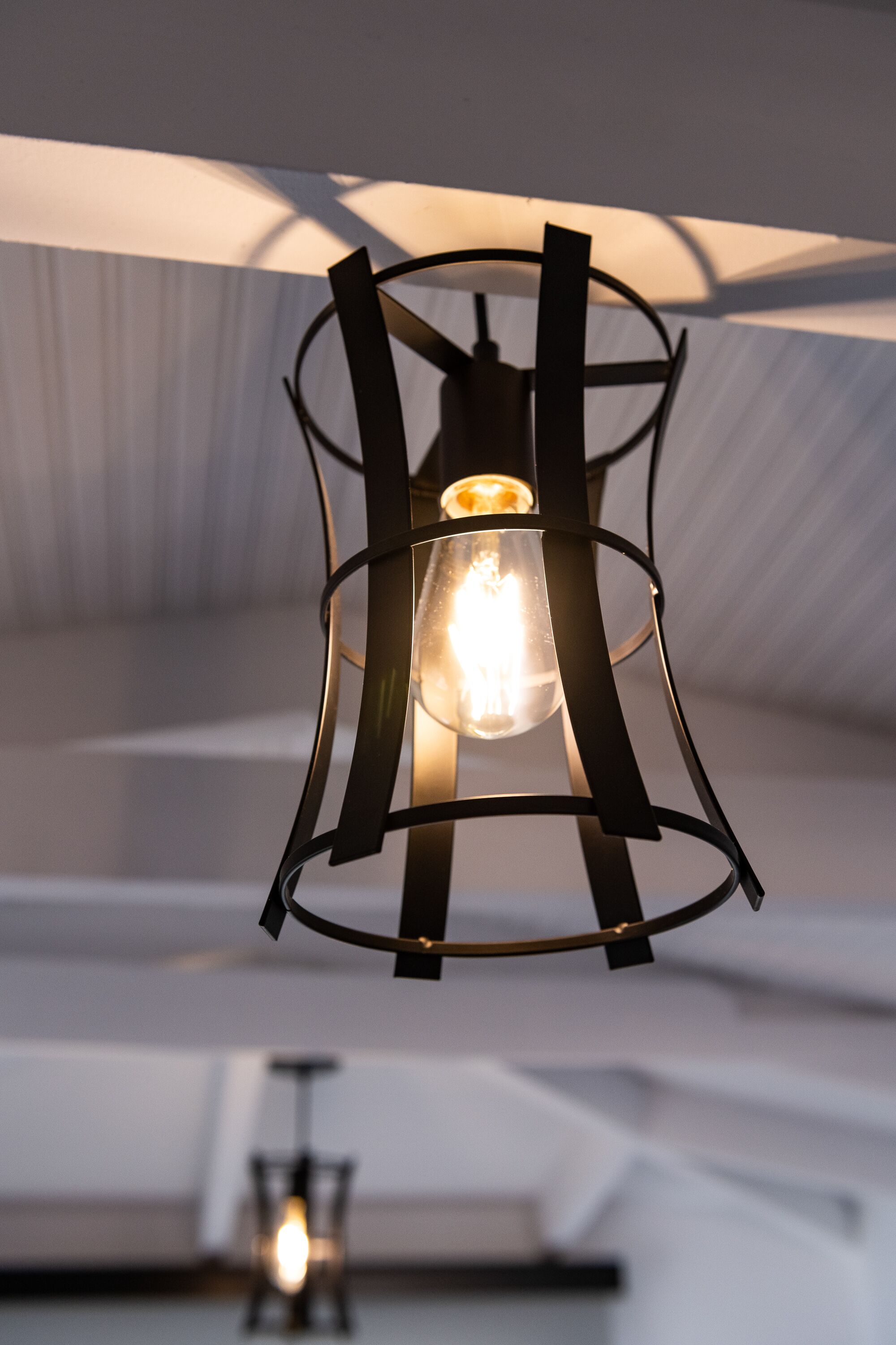 Un candelabro moderno con una estructura metálica y un revestimiento cilíndrico de vidrio, colgado de un techo con diseño acanalado.