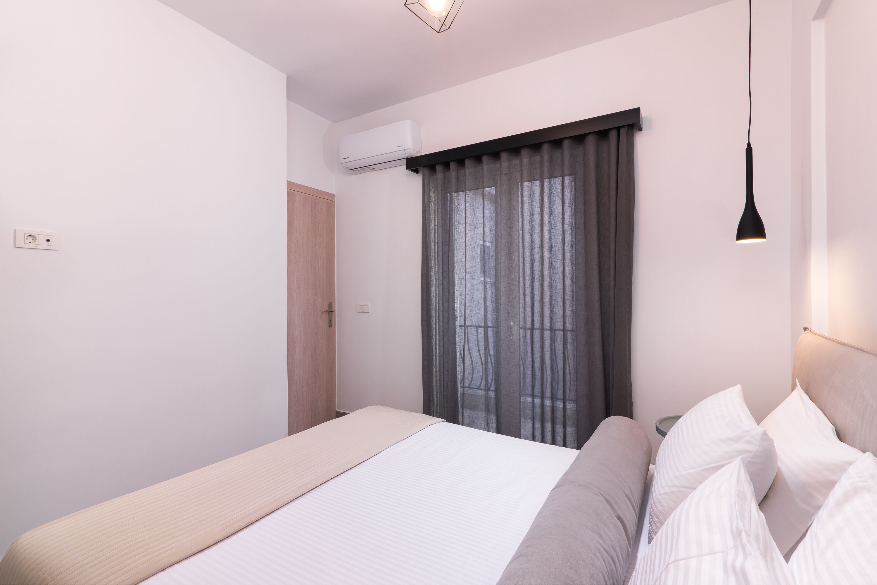 Un dormitorio moderno con cama, mesitas de noche, equipo de aire acondicionado y ventana con cortinas.