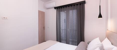 A modern bedroom with a bed, bedside tables, an air conditioning unit, and a window with curtains.