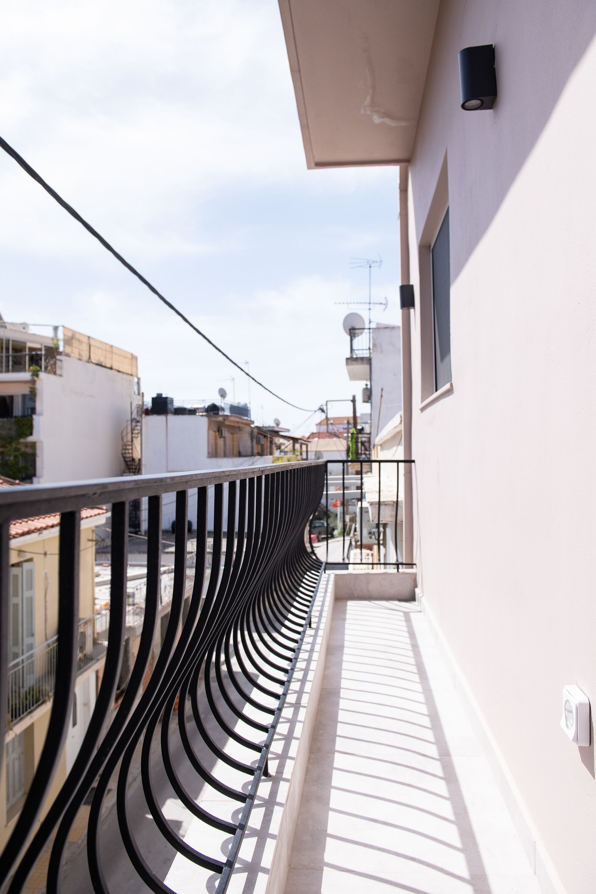 A balcony with a curved black railing, a white wall, and a clear sky in the background.
