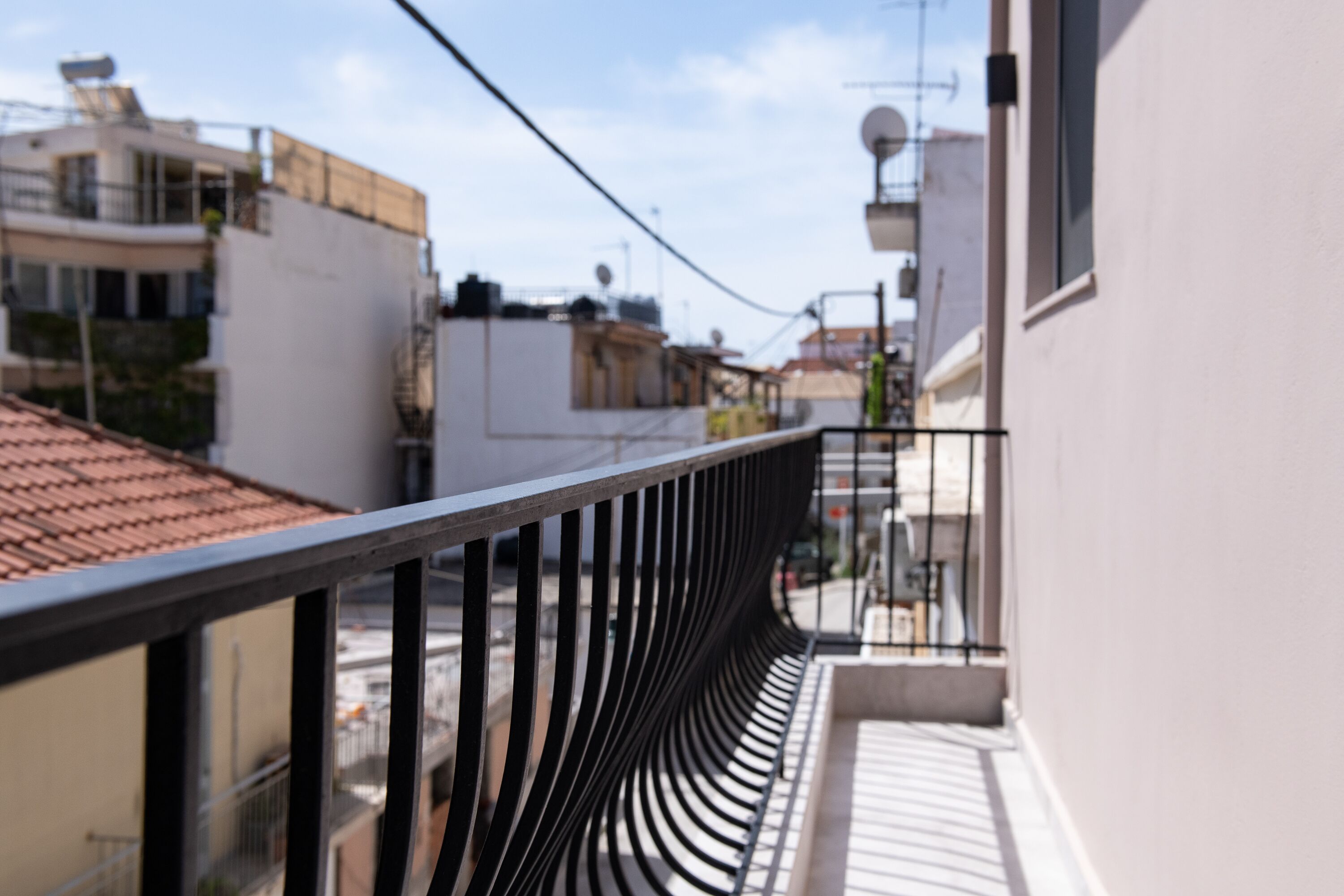 Een balkon met een gebogen zwarte balustrade, met uitzicht op een straat met gebouwen en een heldere lucht.