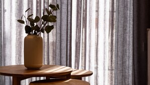A wooden table with a vase of green plants, set against a backdrop of sheer curtains. - Lithies Zante Living (Zakynthos)
