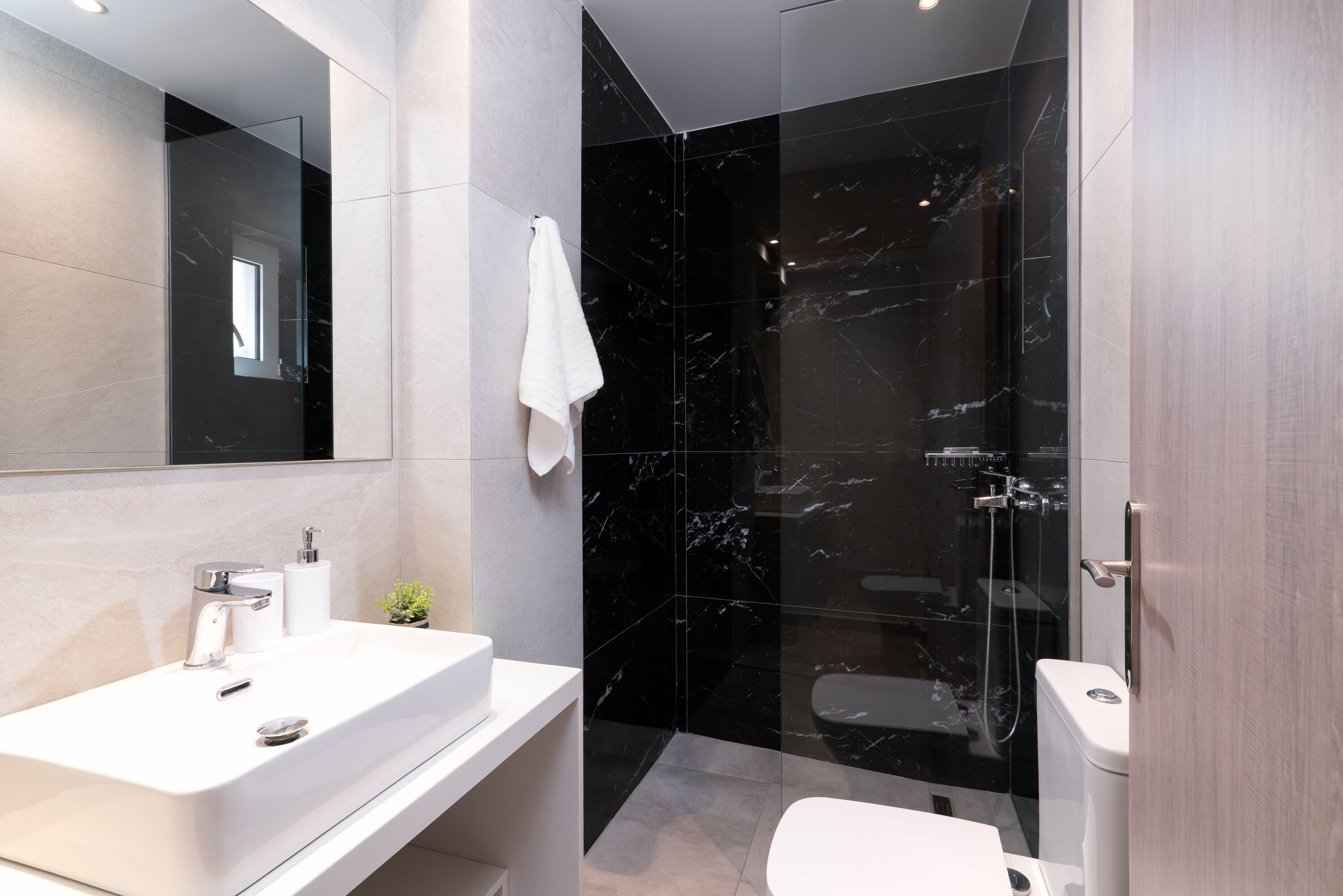 A modern bathroom with a white sink, a mirror, a glass shower enclosure, and a toilet.