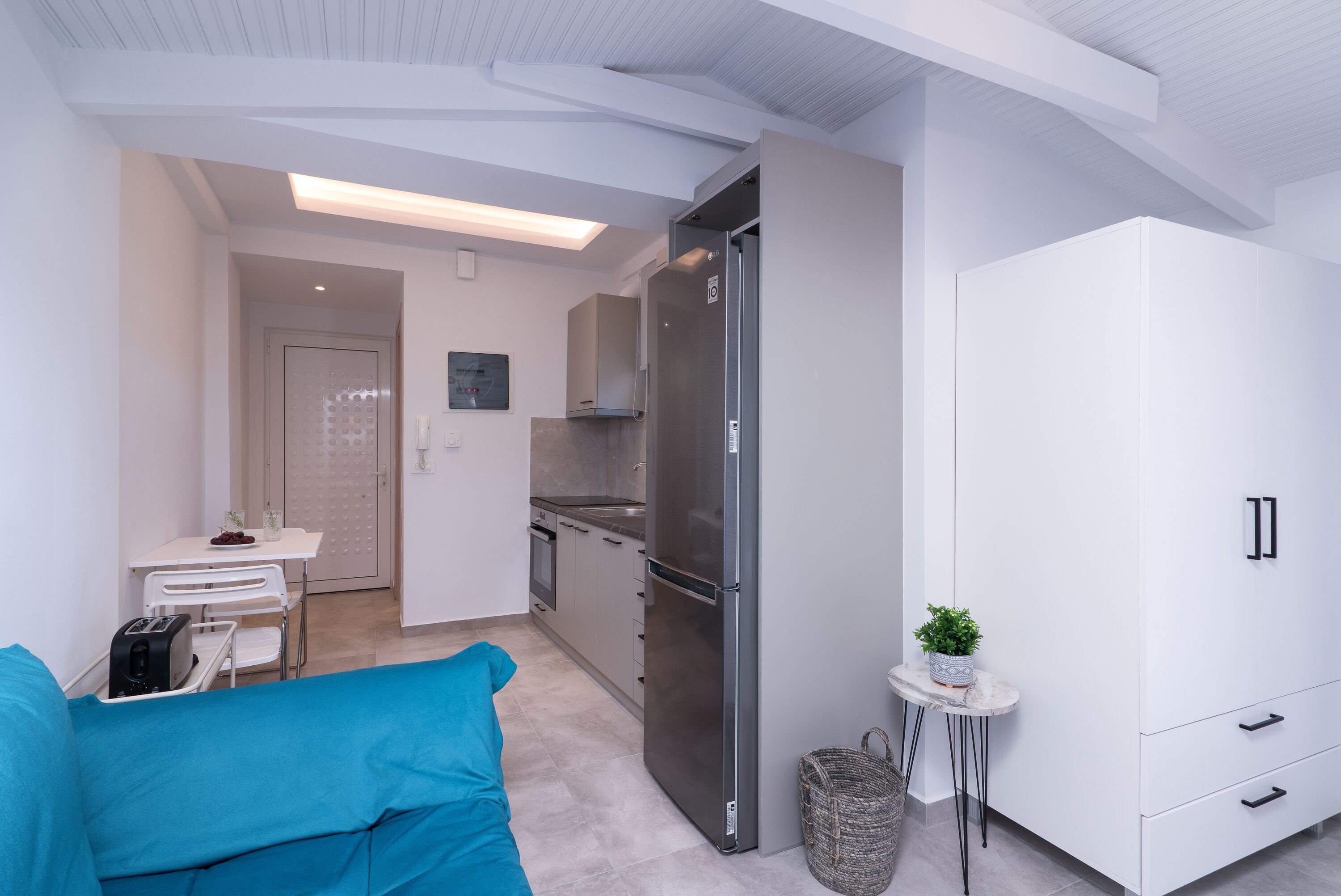 A modern kitchen with white cabinets, a stainless steel refrigerator, and a small table with a plant.