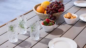 A table with a wicker basket containing fruits and grapes, a bowl of strawberries, and two clear glasses with herbs.