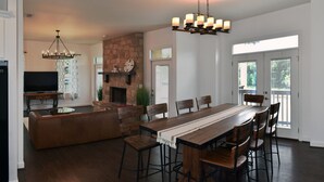 Ein geräumiges Wohnzimmer mit großem Holzesstisch, bequemen Sitzgelegenheiten, einem Kamin und einem Fernseher.