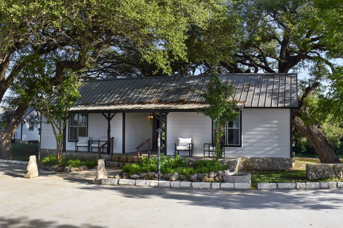 A small, single-story building with a porch, surrounded by trees.