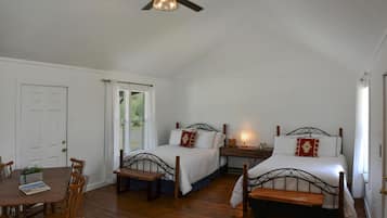 A bedroom with two beds, a ceiling fan, a wooden table with chairs, and a window with curtains.