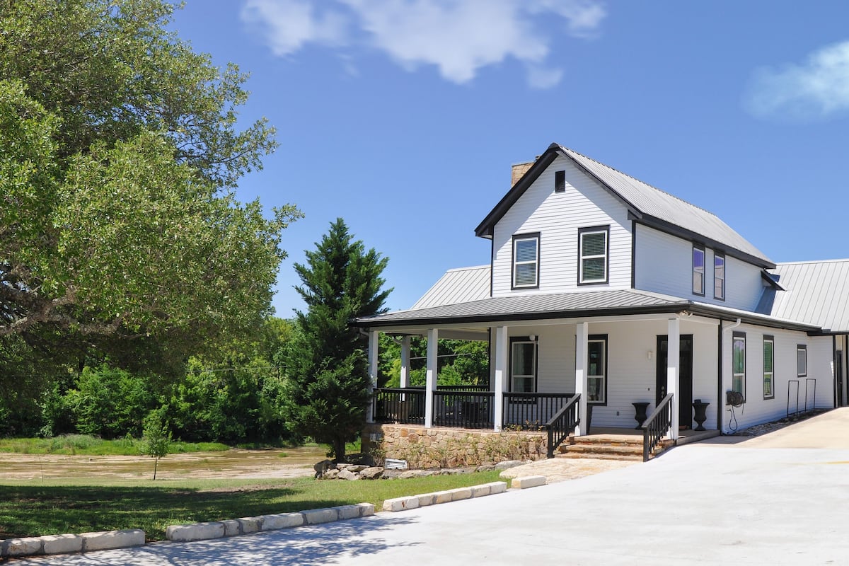 A two-story house with a porch, a stone foundation, and a clear sky.