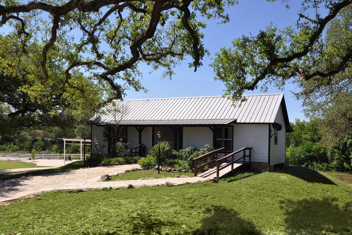 A small, single-story building with a sloped roof, a porch with a wooden railing, and a stone pathway leading to it.