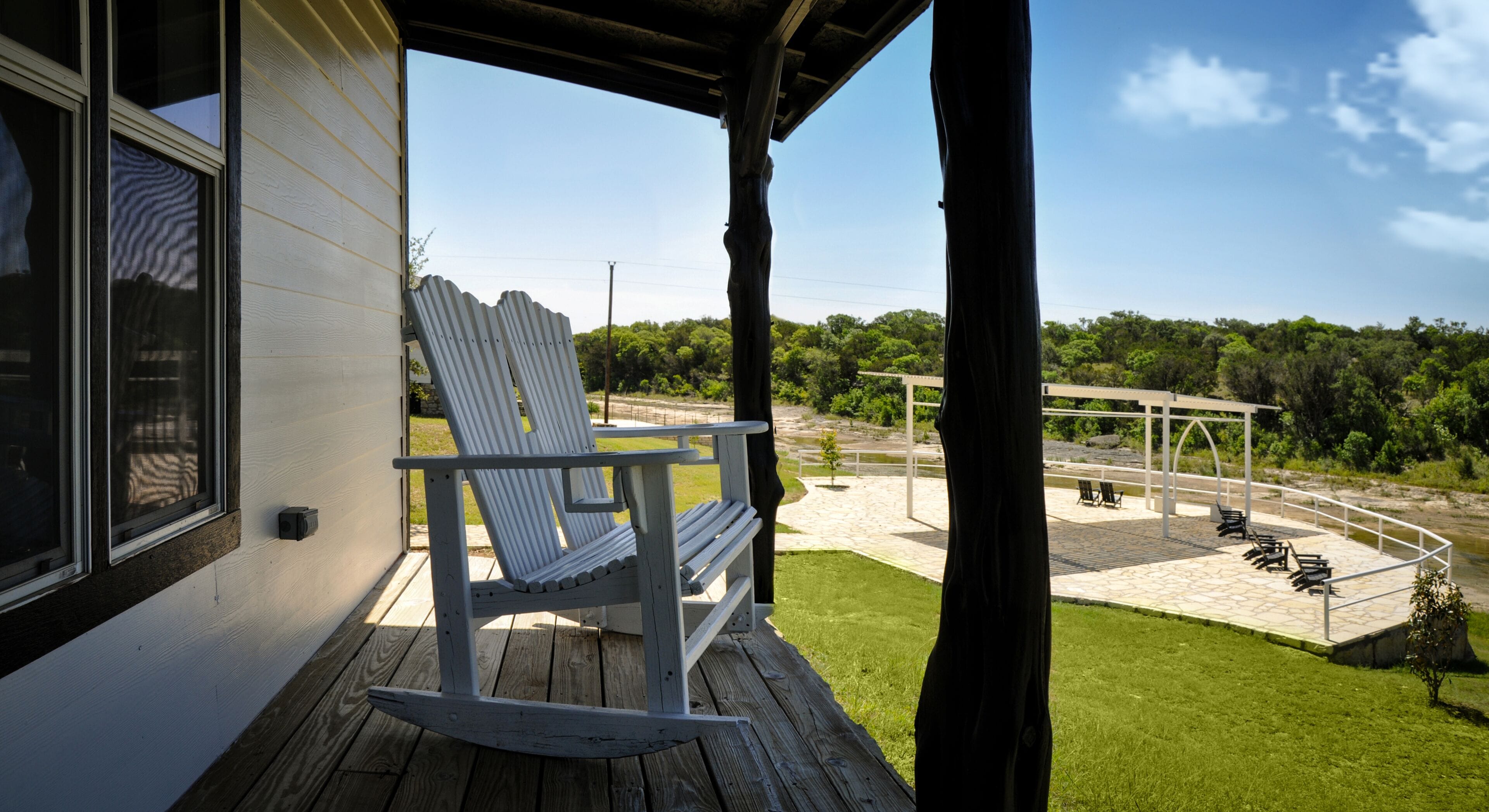 A wooden deck with a rocking chair, a covered patio area, and a view of a park with trees and a gazebo.