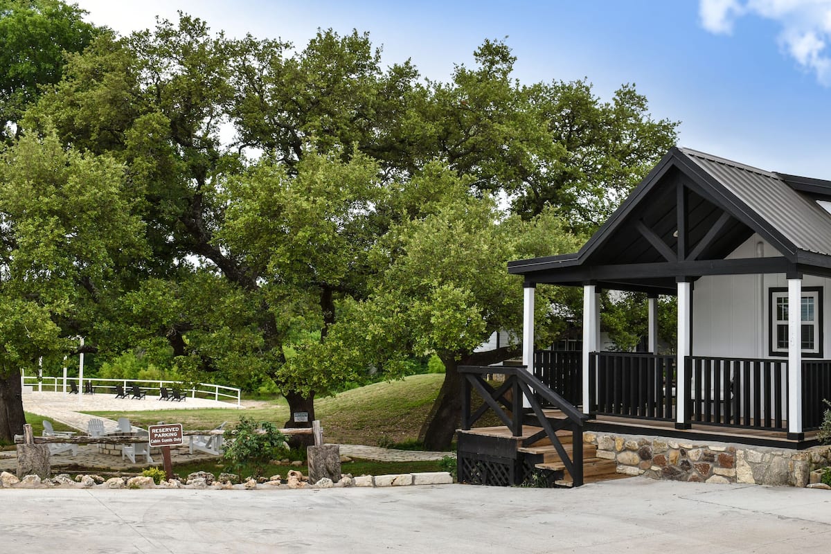 A two-story house with a porch, surrounded by trees and a stone wall.