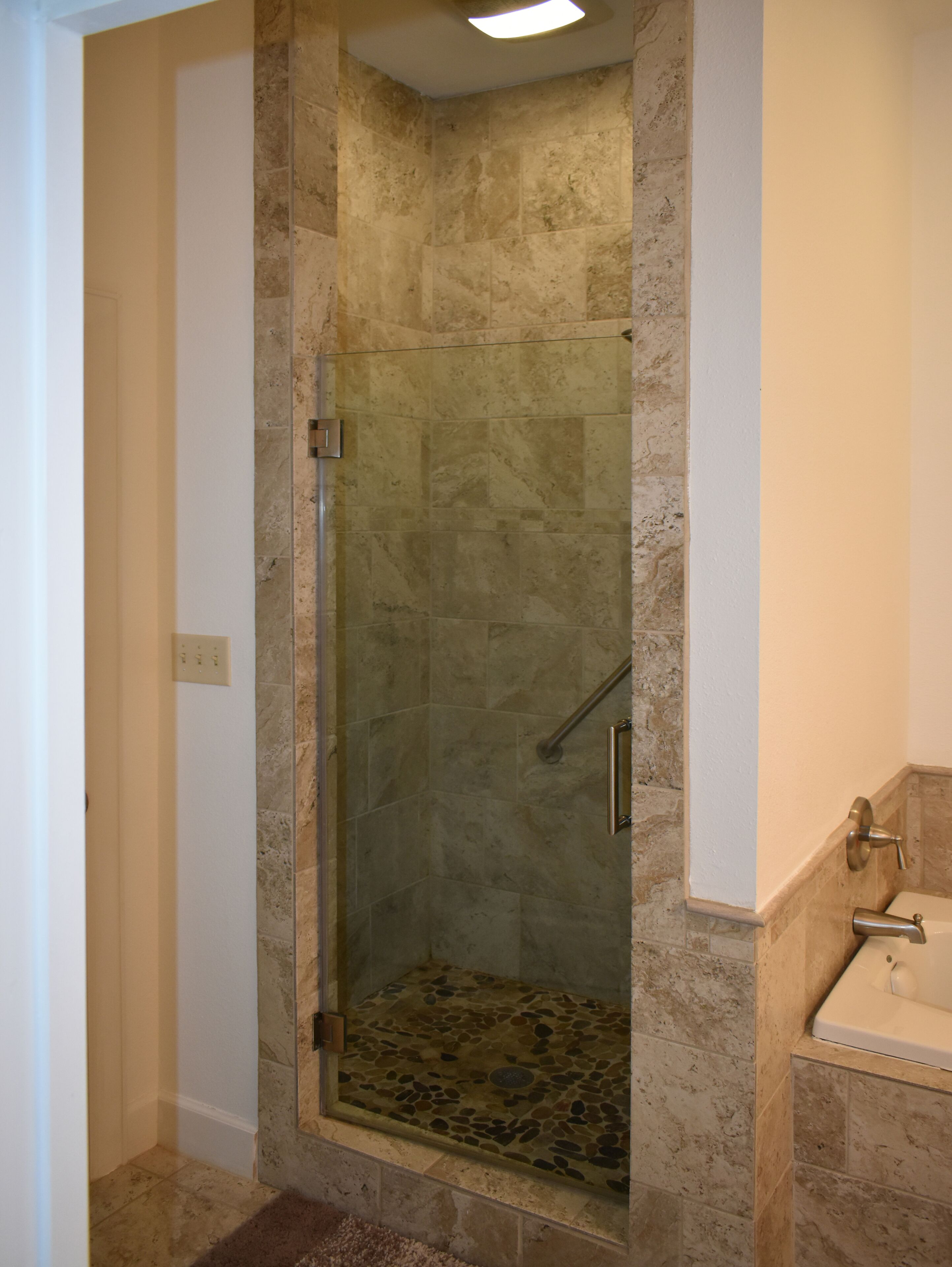 Une douche fermée par des parois de verre, avec un sol en pierre et un lavabo blanc sur le côté droit.