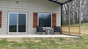 Et moderne hus med en overdækket terrasse, skydedøre og et træhegn.