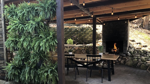 Un patio exterior con suelo de piedra, una mesa y sillas de madera, una pared de piedra y un brasero.