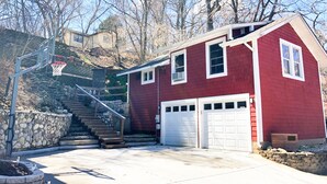 Una casa roja con garaje, aro de baloncesto y una escalera de piedra que sube una colina.
