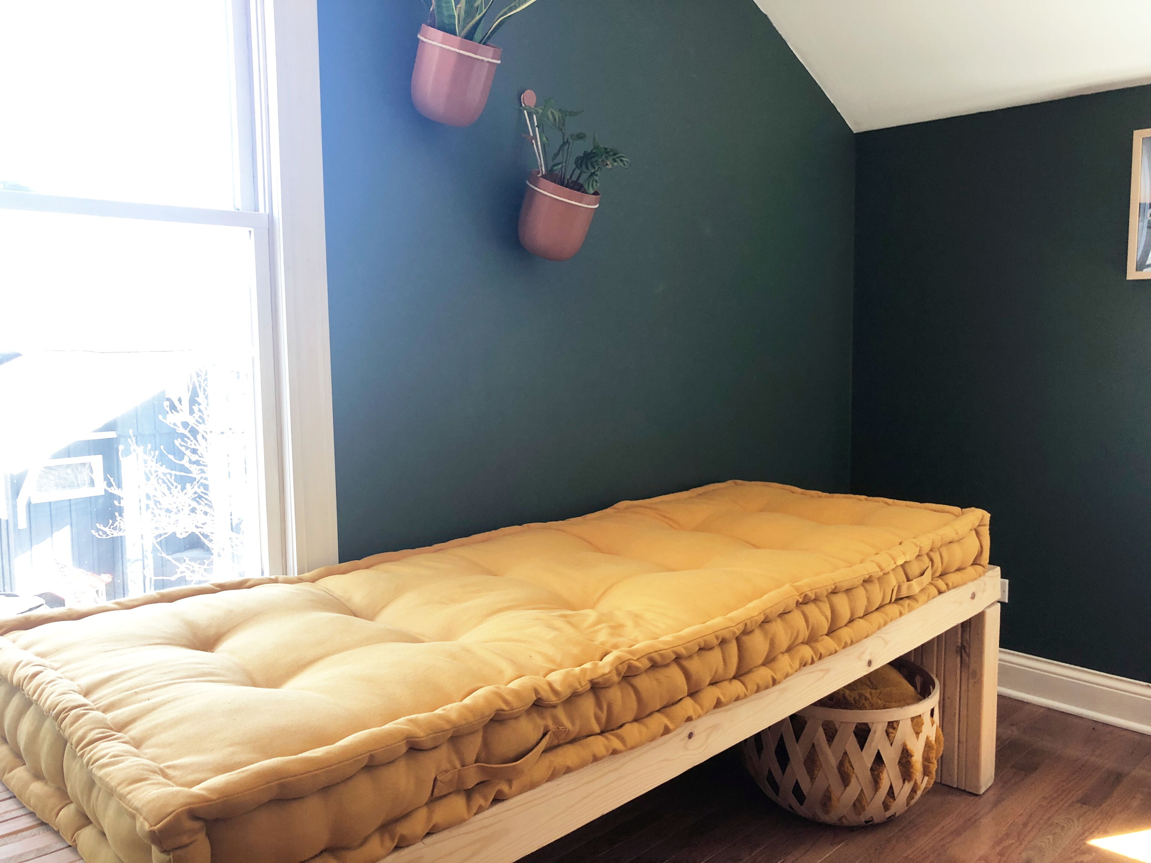A room with a bed, a dark wall, and two hanging potted plants.