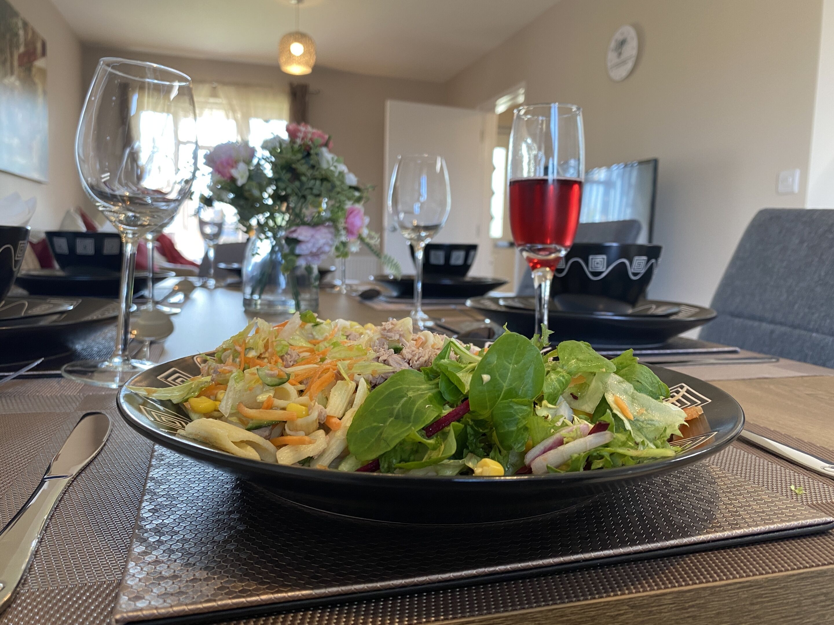 A dining table with a salad, wine glasses, and a vase of flowers.