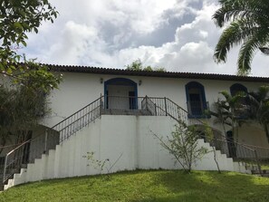 Un bâtiment à l’extérieur blanc, avec des portes bleues et un escalier menant à un étage supérieur.