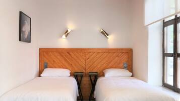 Quarto com duas camas, cabeceira de madeira, duas mesas de cabeceira, um quadro na parede e uma janela.