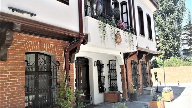 Un edificio de dos pisos con fachada blanca, un balcón lleno de flores y una entrada de ladrillo.