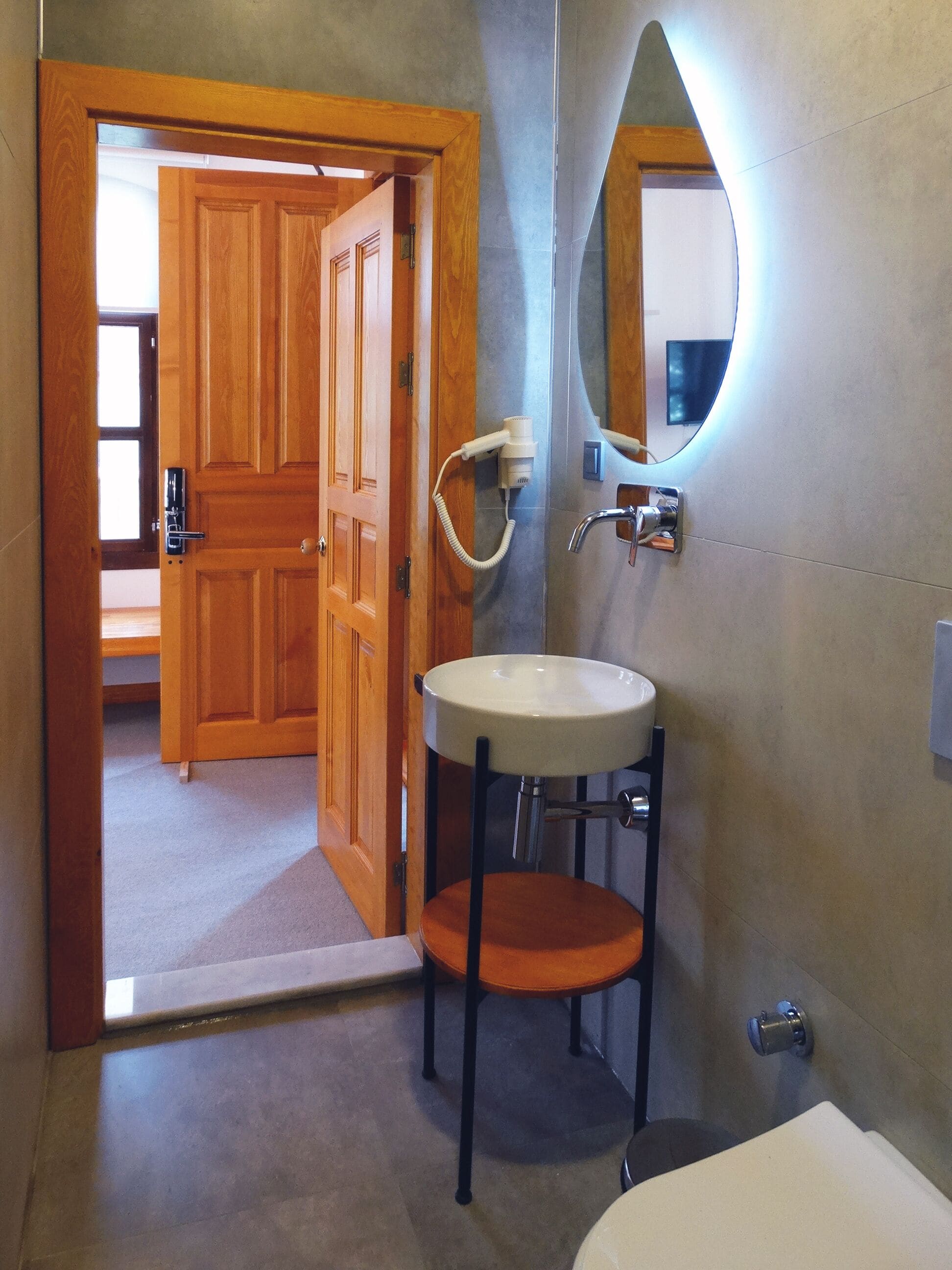 A bathroom with a wooden door, a sink with a mirror, and a shower area.