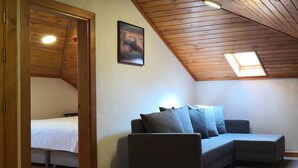 Una habitación acogedora con techo de madera, un sofá gris con cojines, una cama con ropa de cama blanca y un tragaluz.