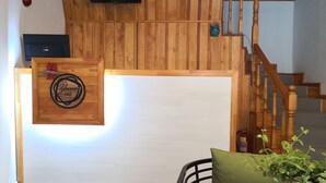 Un interior de madera con un televisor montado, un letrero de madera que dice 'Yuva hotel', una escalera y un comedor con mesa y sillas.