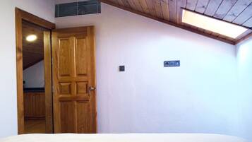 A bedroom with a wooden door, a bed, a ceiling vent, and a light switch on the wall.