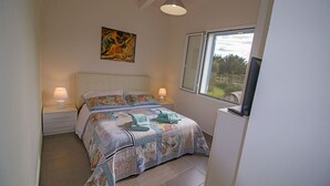 Ein Schlafzimmer mit einem Bett, zwei Nachttischen, einem Bild an der Wand, einem Fenster mit Blick und einem Fernseher auf einem Schrank.