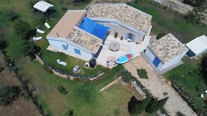 Eine Vogelperspektive zeigt ein Haus mit einer großen Terrasse, einem Swimmingpool und einem separaten Gebäude mit blauem Dach.