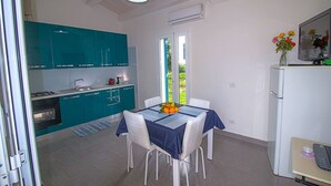 Eine kompakte Küche mit türkisfarbenen Schränken, einem Esstisch mit blauer Tischdecke und einem Kühlschrank.