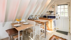 A cozy kitchen with a wooden table, bar stools, and a window overlooking the garden. - Blue Bell (Corsham)