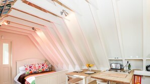 A cozy, well-lit attic bedroom with a bed, a small table, and a kitchenette. - Blue Bell (Corsham)