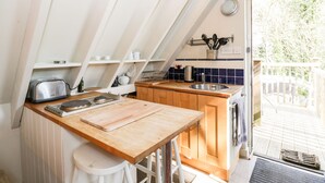 A kitchen with a wooden countertop, a sink, and a toaster. There are shelves above the counter and a window to the right. - Blue Bell (Corsham)