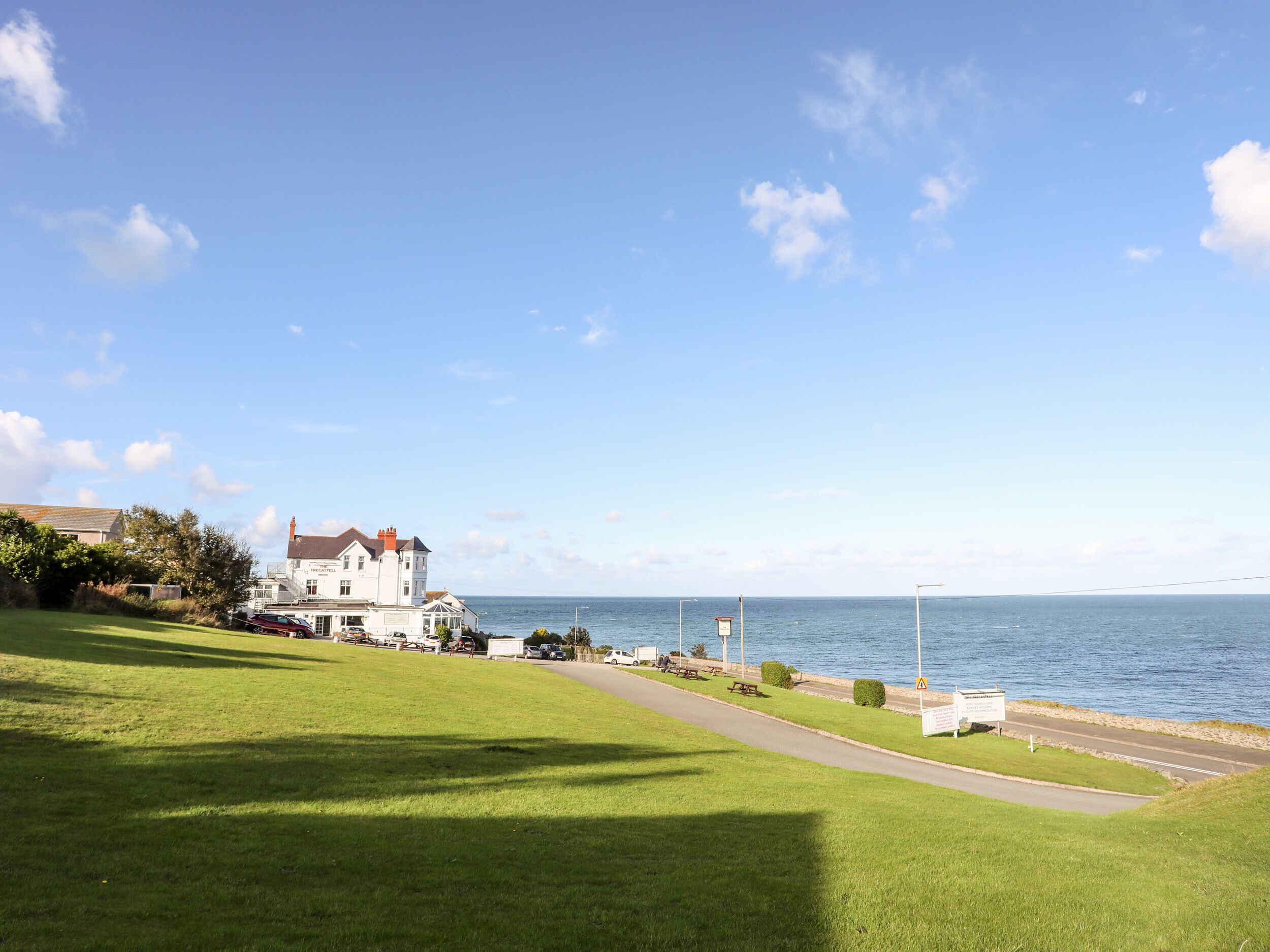 A coastal property with a large house, a grassy lawn, a road, and a view of the sea.